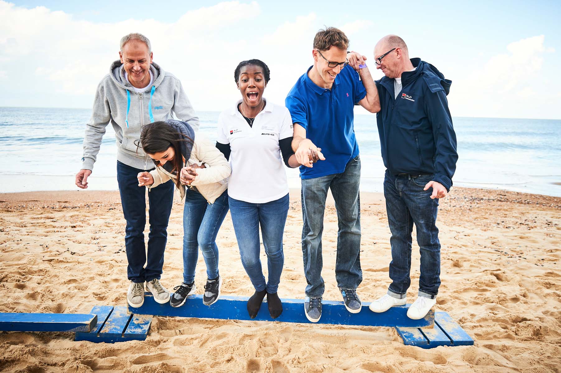 participants on a beam carrying out hand in hand an event of the Beach & Water Olympics