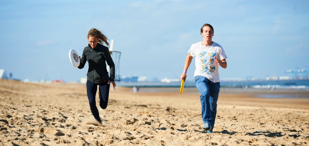 participants running on the beach with a frisbee in hand during the Beach & Water Olympics