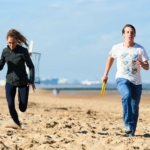 participants running on the beach with a frisbee in hand during the Beach & Water Olympics